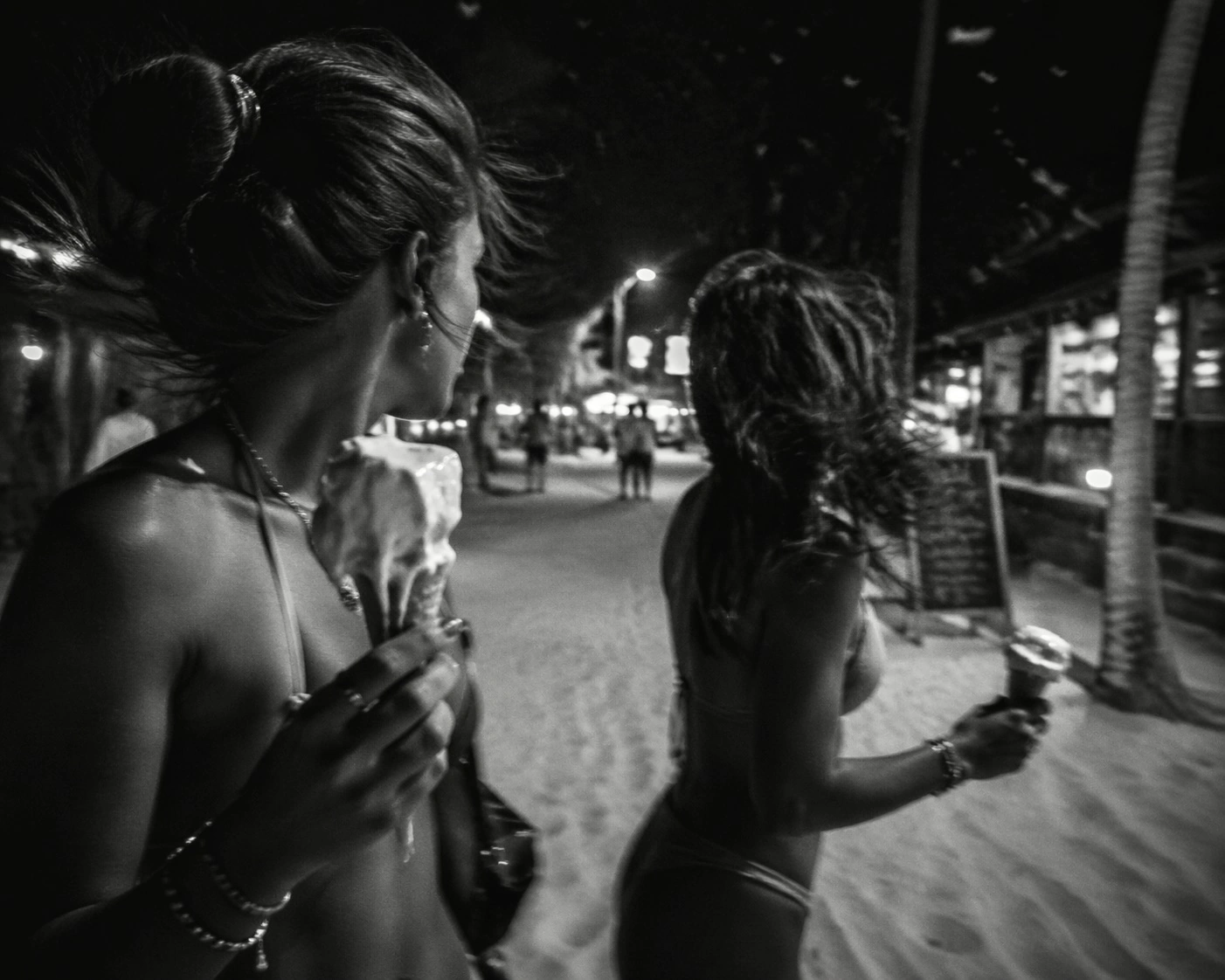 La rue principale de Jericoacoara la nuit, en noir et blanc, des gens pieds nus dans le sable