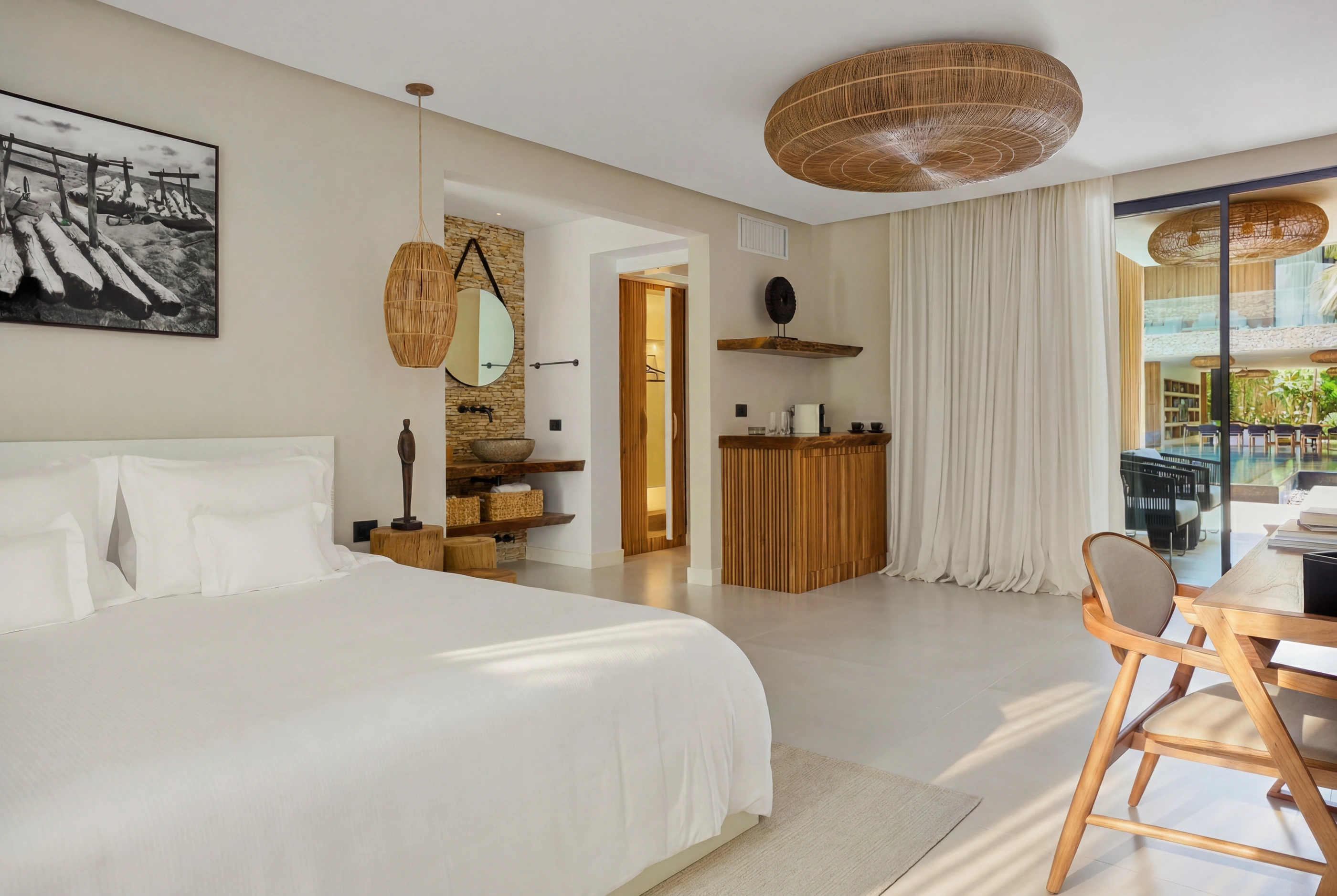 White-linen bed with a round mirror and stone vanity, opening to the pool and dining view.